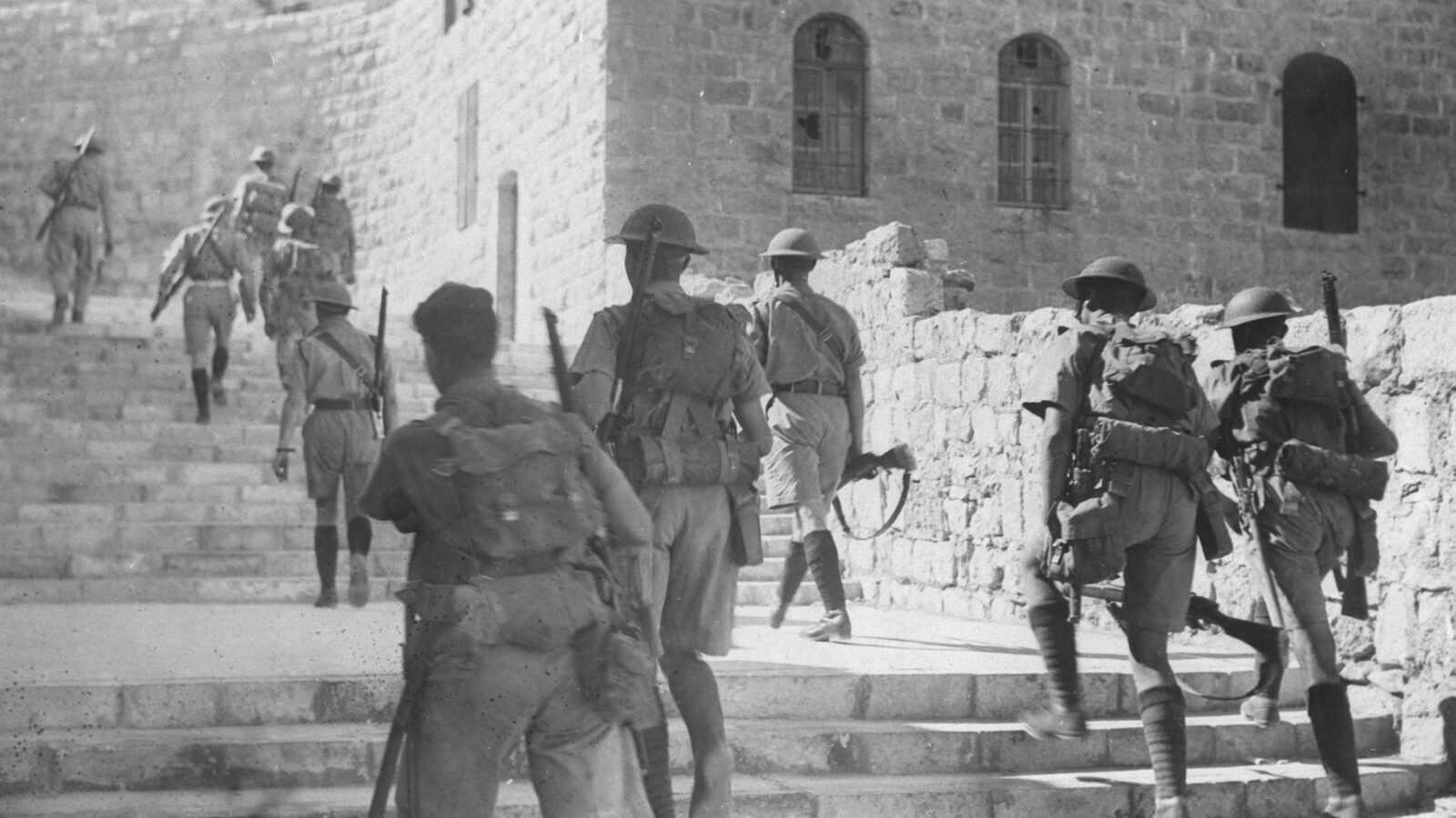 Armed British soldiers in steel helmets climb the stone steps of the Old City of Jerusalem to impose a curfew, October 1938